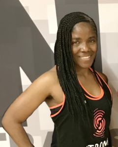 A woman with long dark braids smiling and wearing a Zumba Strong tank top.