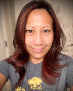A woman with dark red and brown hair grinning and wearing a UMBC T-shirt.
